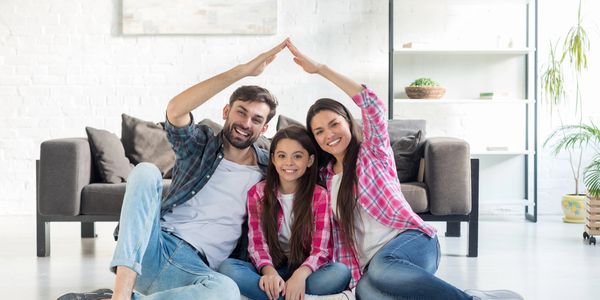 Happy family sitting on the floor making a roof shape with their hands.
