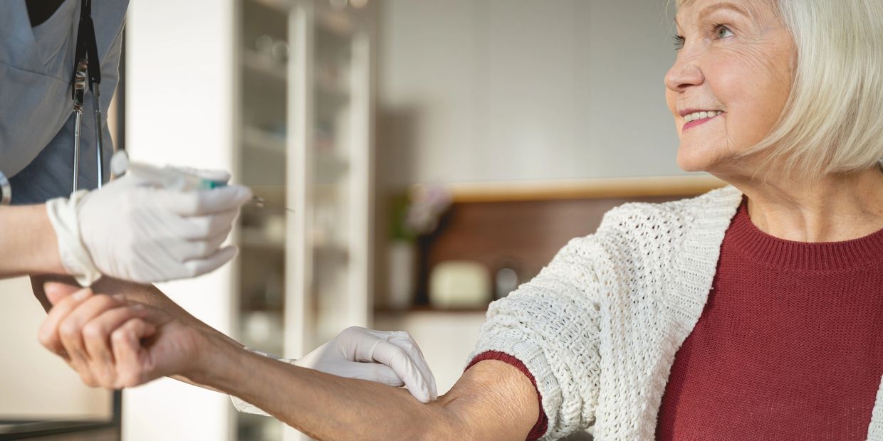 Elderly woman smiling while receiving a vaccine injection from a healthcare professional.