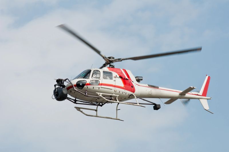 A helicopter equipped with a camera hovering in the sky in Yokohama, Japan. The fuselage colored in red and white is used  by the press to report from the sky. Low angle view of the copter against blue sky with white cloud.