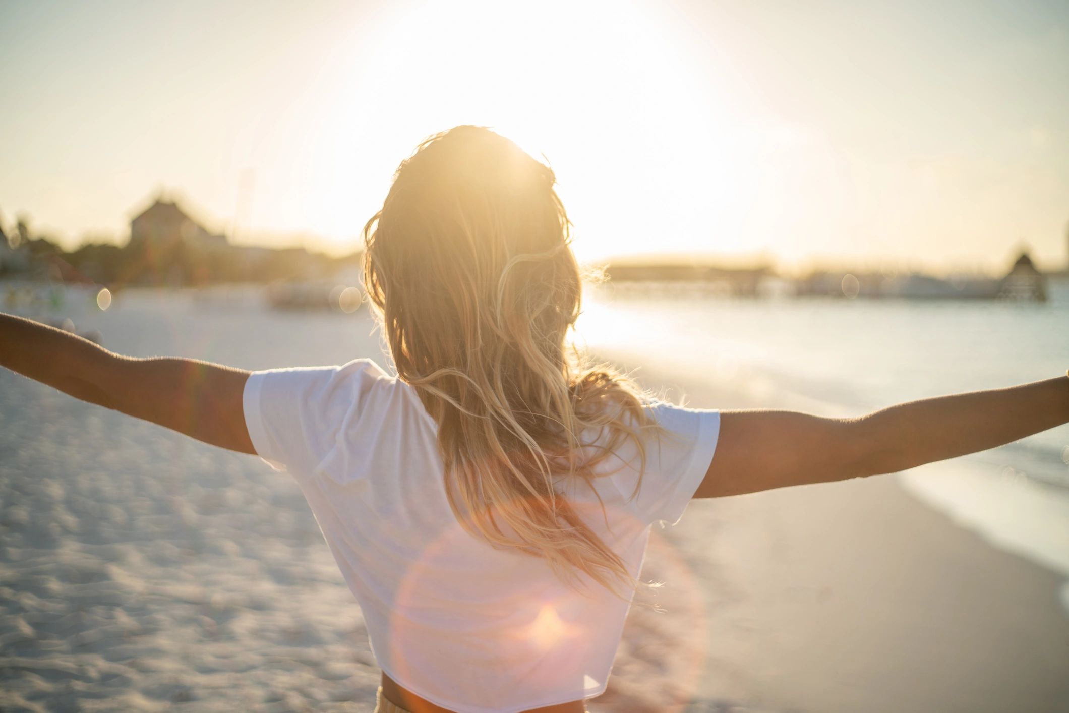 Person with arms outstretched facing the sun on a beach.