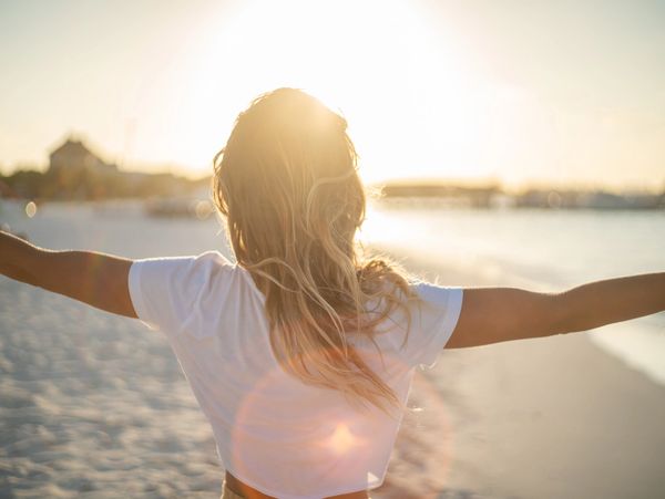 Person with arms outstretched enjoying a sunny beach at sunset.