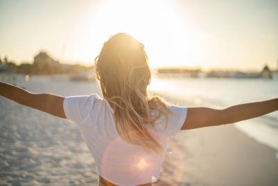 Woman enjoying sunrise at the beach with open arms.