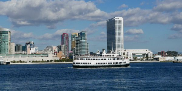 A ferry boat sailing near a city skyline on a sunny day.