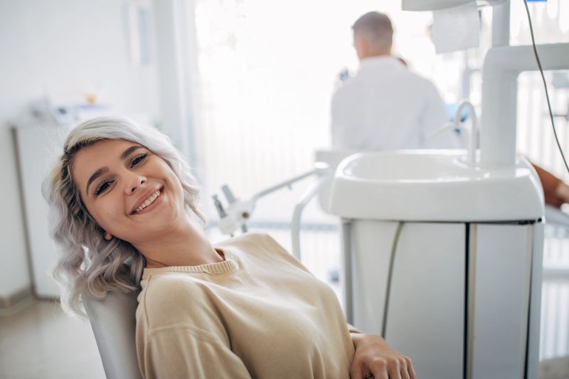 Satisfied dentist patient showing her perfect smile after treatment in a clinic box with medical equipment in the background
