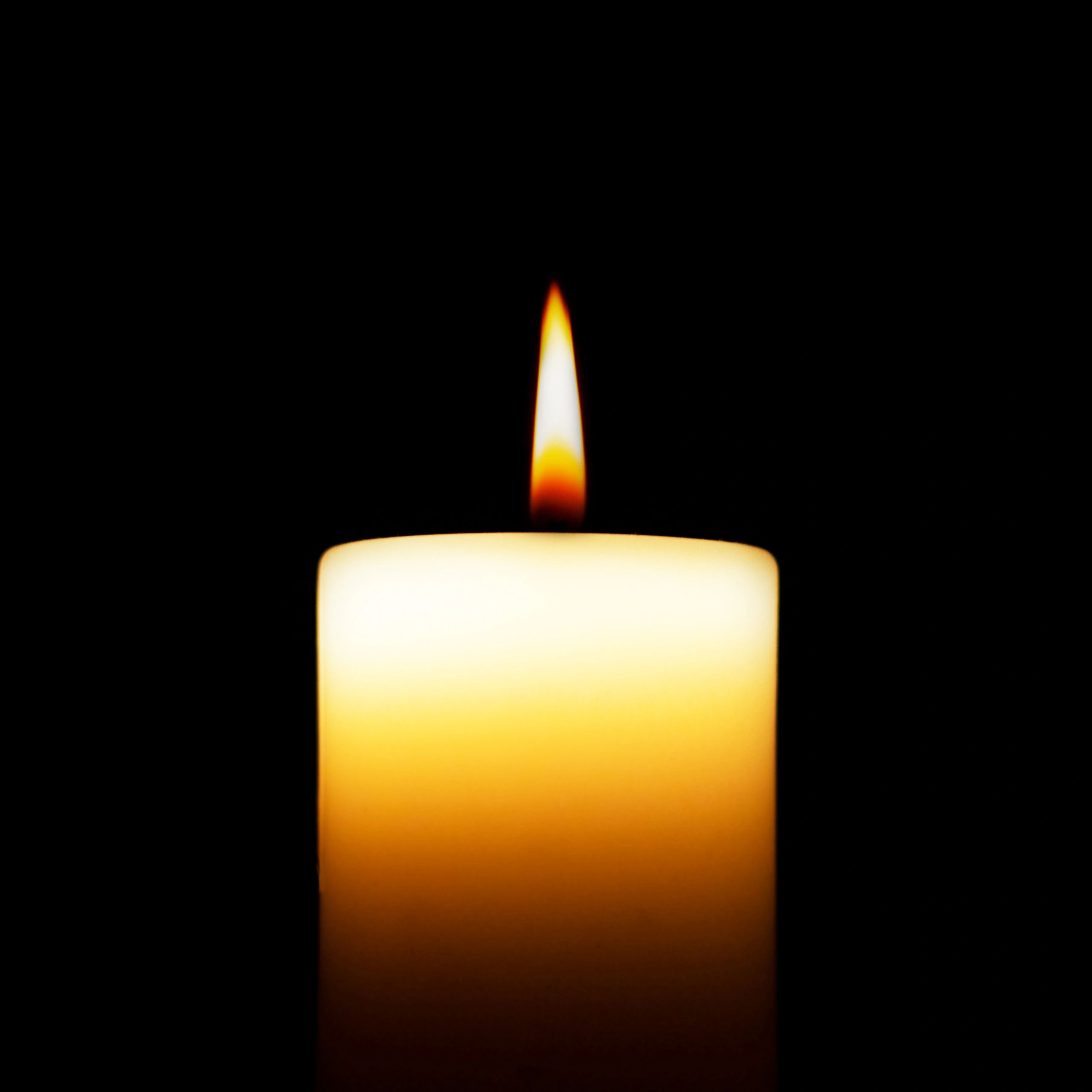 A single lit candle flame glowing against a dark background.