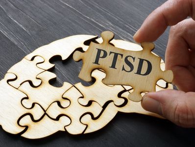 A hand placing a puzzle piece labeled PTSD into a wooden puzzle.