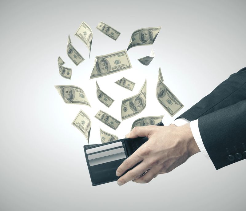 Businessman hand holding purse from which emerge dollars. Business success and financial concept