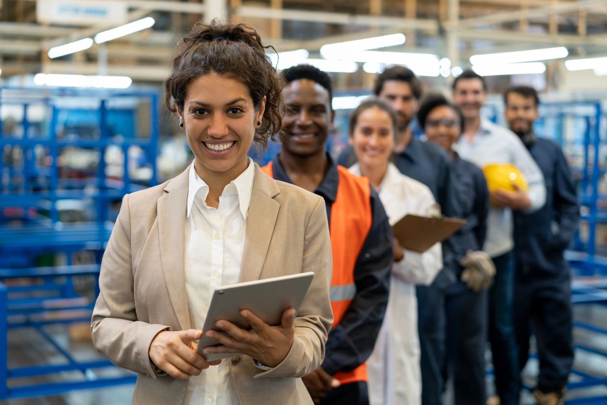 Diverse professionals smiling in a factory setting, showcasing teamwork and leadership.