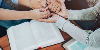 Group holding hands in prayer over open books.
