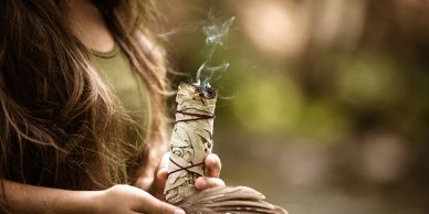 Woman holding a burning sage bundle for cleansing.
