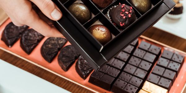 Box of assorted chocolates being held above a tray of dark chocolate pieces.