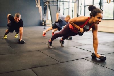 Three people doing dumbbell rows in a plank position at a gym.
