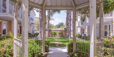 A white gazebo in a sunny garden pathway between residential buildings.