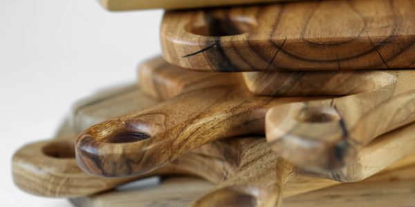 Stack of wooden cutting boards with handles on a white surface.