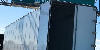 An empty white truck trailer with its door open on a sunny day.
