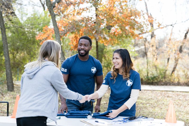 Mid adult woman greets a female volunteer during a community cleanup event. The mid adult woman is working at the volunteer registration table.