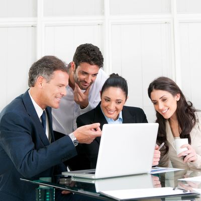 Four professionals collaborating around a laptop in a bright office.