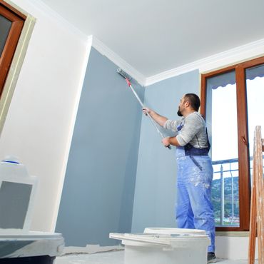 Painter applying blue paint on a wall using a roller indoors.