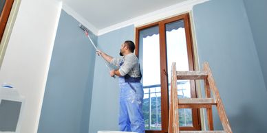 Man painting a room's walls light blue using a roller brush.