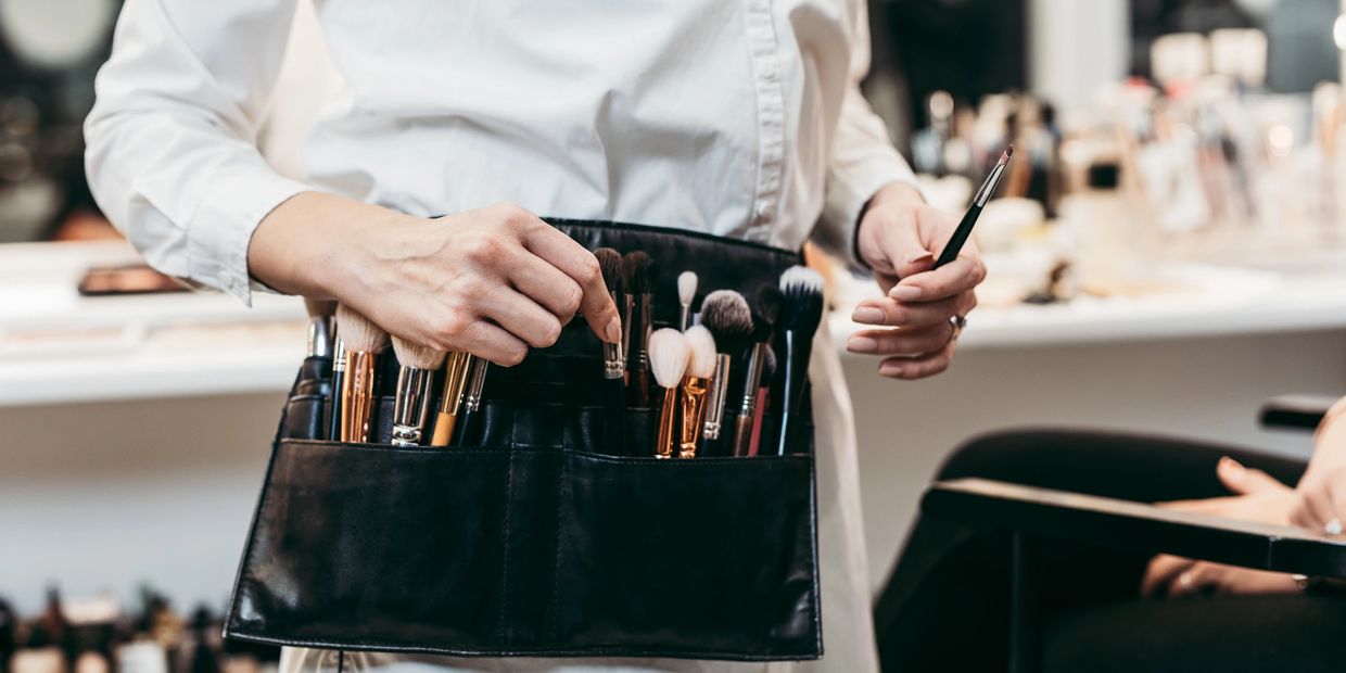 A makeup artist holding a brush holder filled with makeup brushes.