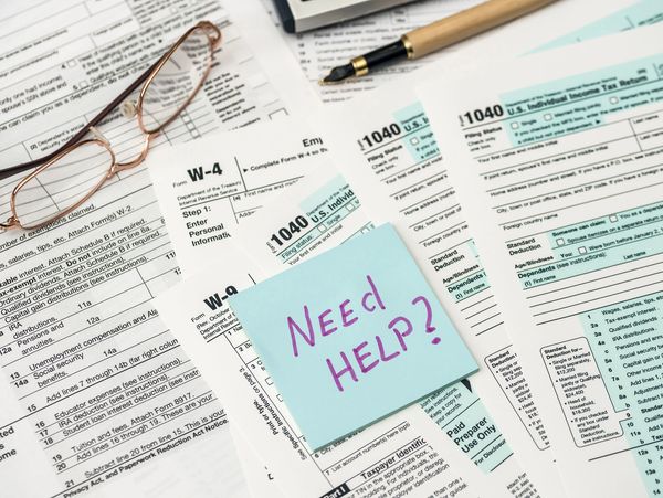Tax forms with a sticky note asking 'Need Help?' and reading glasses.