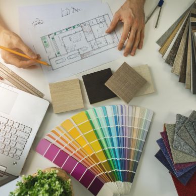 Hands working on a floor plan surrounded by color and material samples.