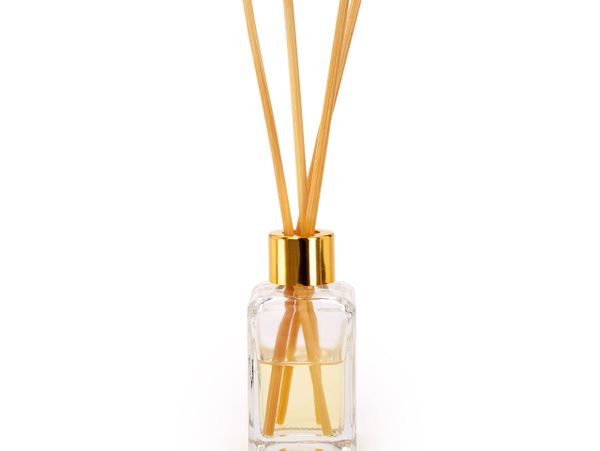 A glass reed diffuser with golden cap and fragrance sticks.