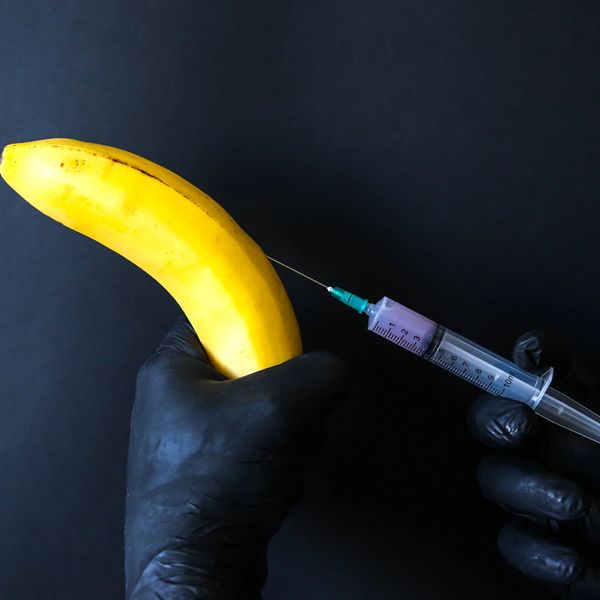 Gloved hands injecting a yellow banana with a syringe filled with purple liquid.