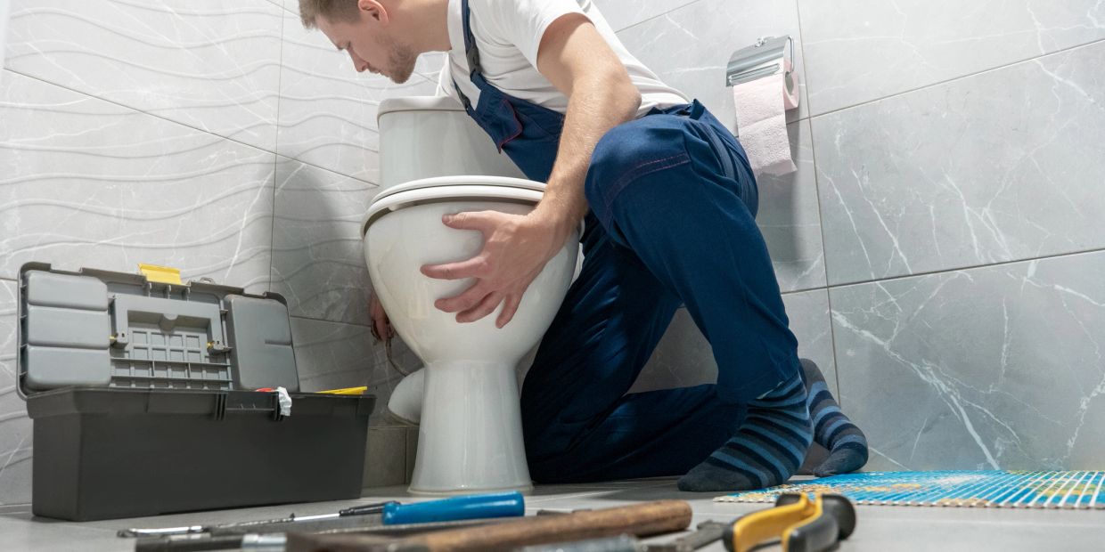 Plumber fixing a toilet with tools in a modern bathroom.