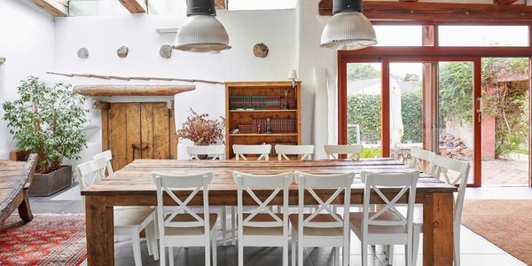 Rustic dining room with a large wooden table, white chairs, and natural light.