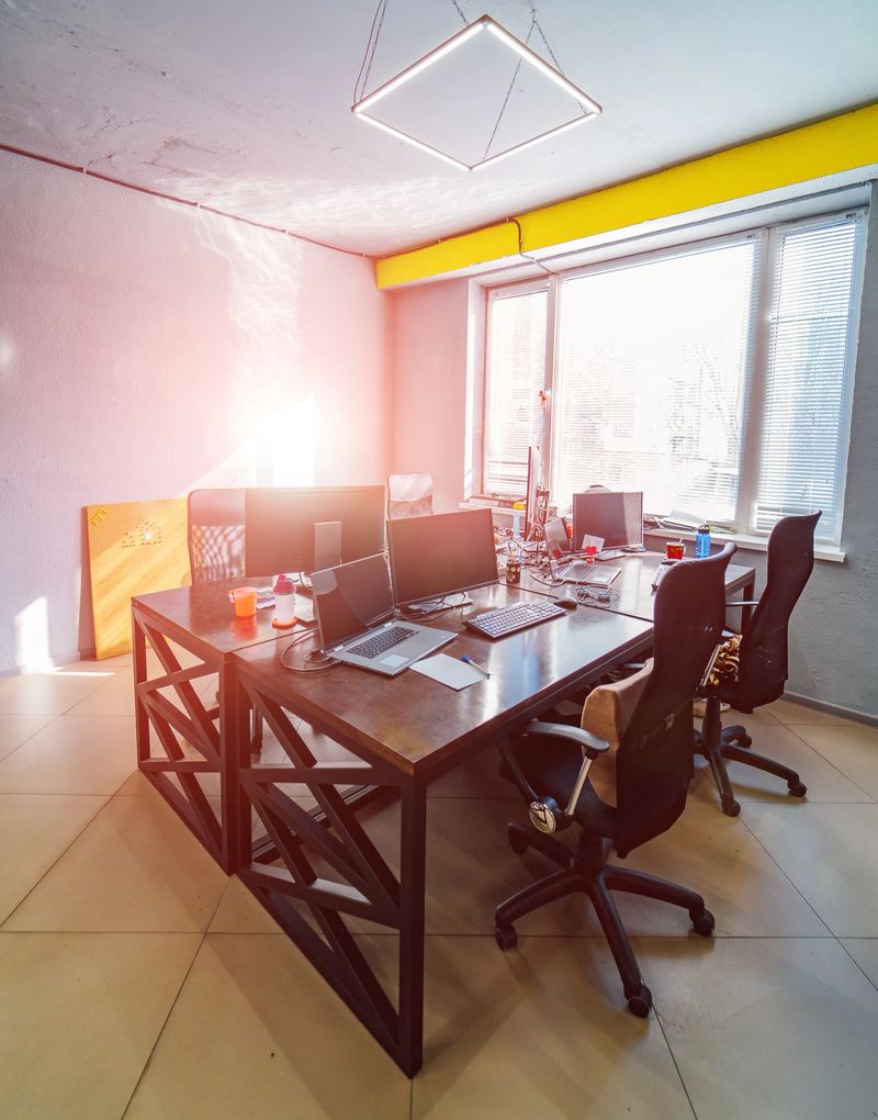 Chairs at wooden modern table with laptops .Wide window and yellow emphasis above it. Bright stickers at blue wall. Office interior concept.