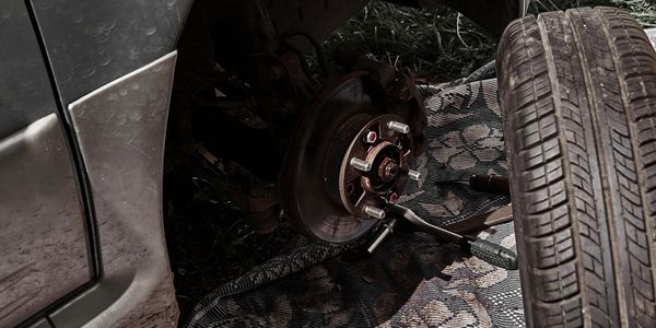 Car wheel removed, showing brake disc and tools on the ground.