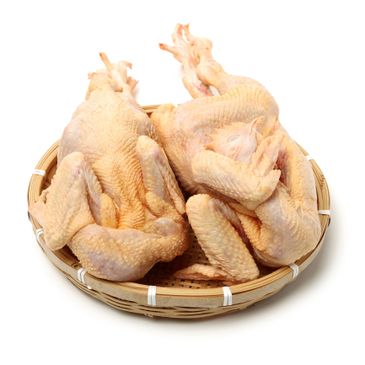 Two whole raw chickens placed in a round bamboo basket.