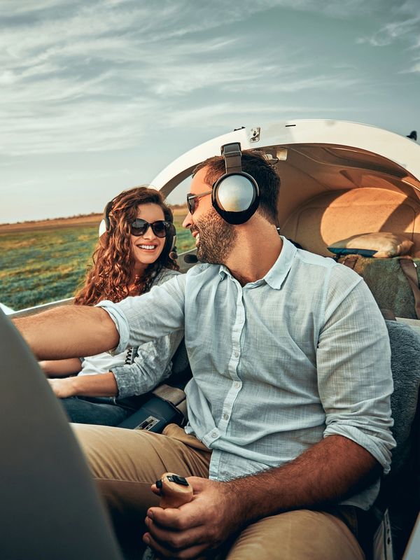 Couple smiling inside a small airplane, wearing headsets and sunglasses.