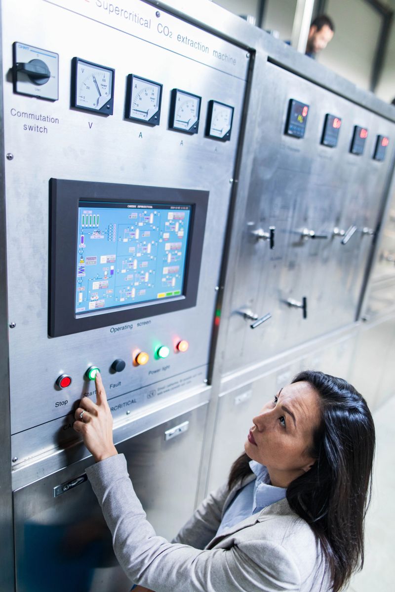Female quality control inspector pressing start button on a machine in a factory.