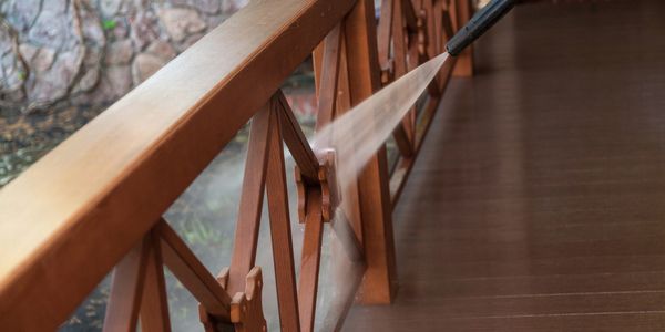 A wooden balcony railing being cleaned with a pressure washer.