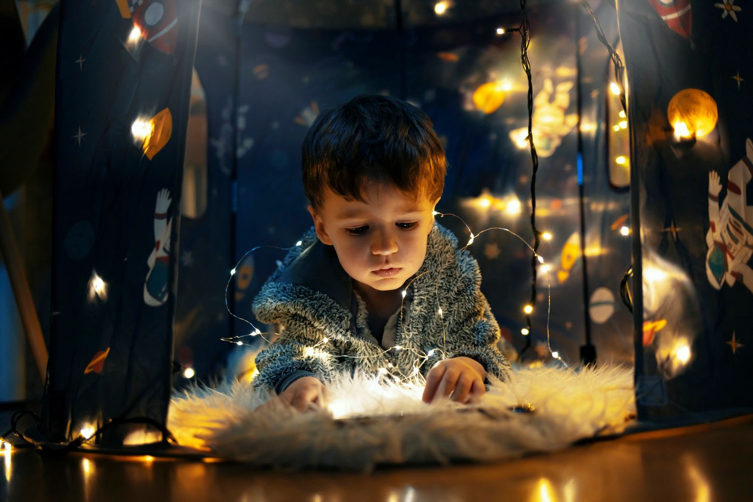 A child surrounded by fairy lights inside a space-themed tent.
