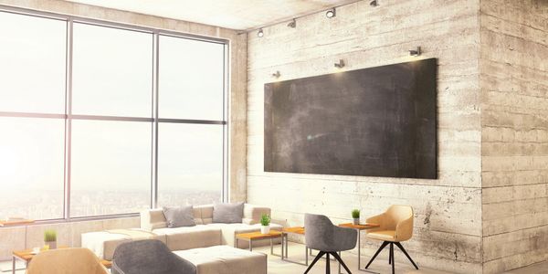 Modern lounge area with chairs, sofas, and a large chalkboard on a concrete wall.
