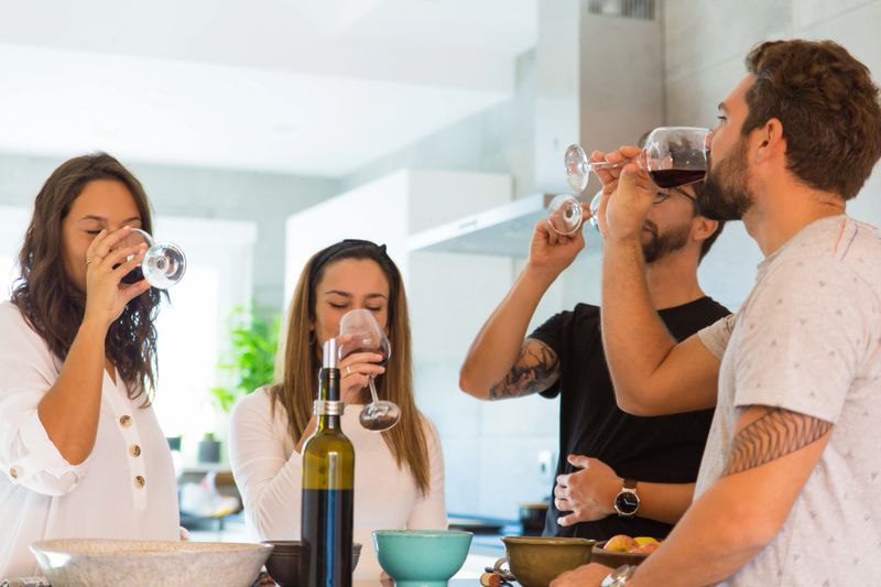 Smiling young friends tasting wine. Group of cheerful people standing near table and drinking wine. Wine tasting concept