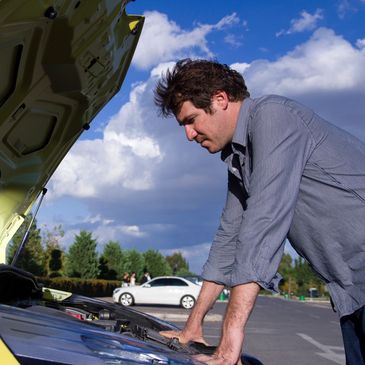 Man examining car engine with hood open on a sunny day.