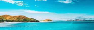 Clear blue water with green hills under a bright sky.
