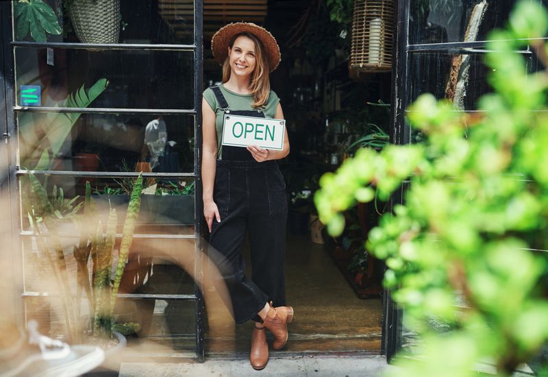 Full length portrait of an attractive young business owner standing alone and holding the open sign at the floristry entrance