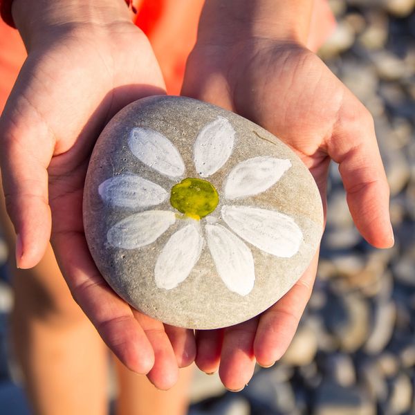 Hands holding a stone painted with a white flower.