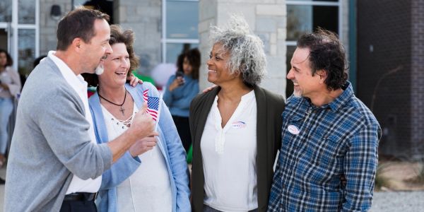 Four people happily talking outdoors, one holding a small American flag.