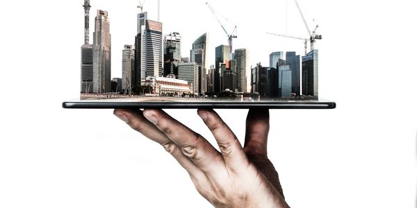 Hand holding a tablet with a miniature cityscape and cranes emerging from it.