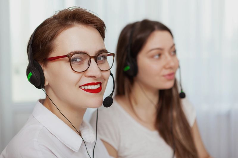 Cheerful female customer service agent wearing headset with microphone, smiling to the camera. CHarming women working at call center