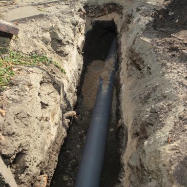 Trench with a black pipe laid underground for utility installation.
