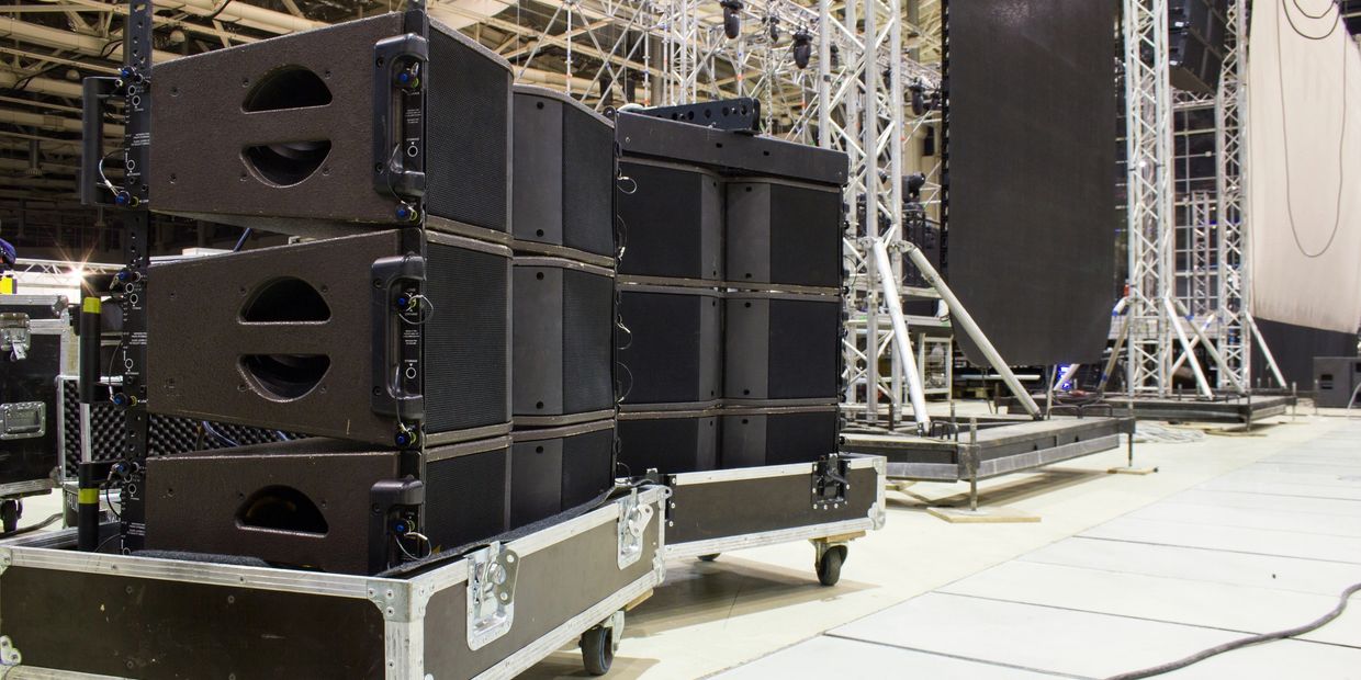 Stacked professional speakers and sound equipment on wheels in a large indoor venue.