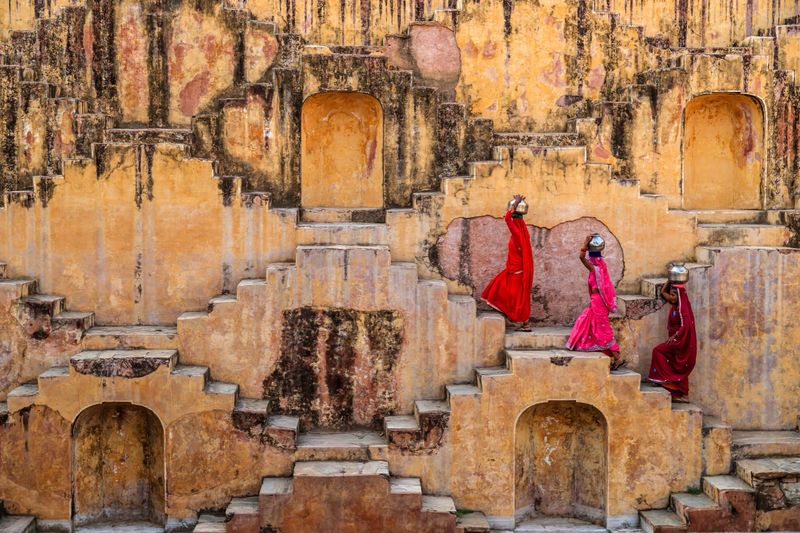 Indian women carrying water from stepwell near Jaipur, Rajasthan, India. Women and children often walk long distances to bring back jugs of water that they carry on their head. Stepwells are wells in which the water may be reached by descending a set of steps.