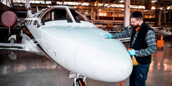 Man cleaning the nose of a small private jet in a hangar.